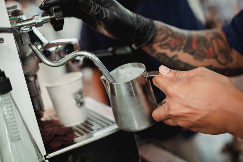 Espresso machine steam wand texturing milk in a stainless pitcher