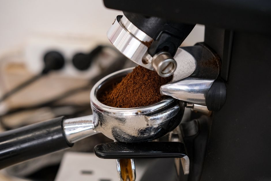 Fresh ground coffee dosing from the grinder chute into a stainless portafilter
