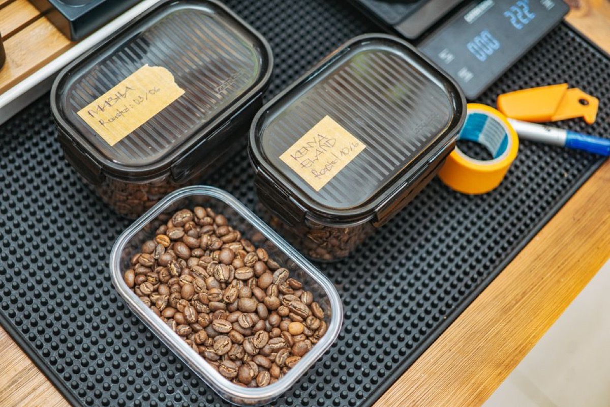 Three labeled airtight storage containers with coffee beans and roast dates on a barista counter