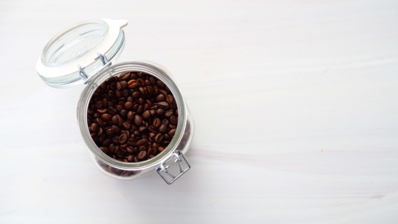 Open airtight glass jar with a flip-top wire-bail lid filled with dark roasted coffee beans