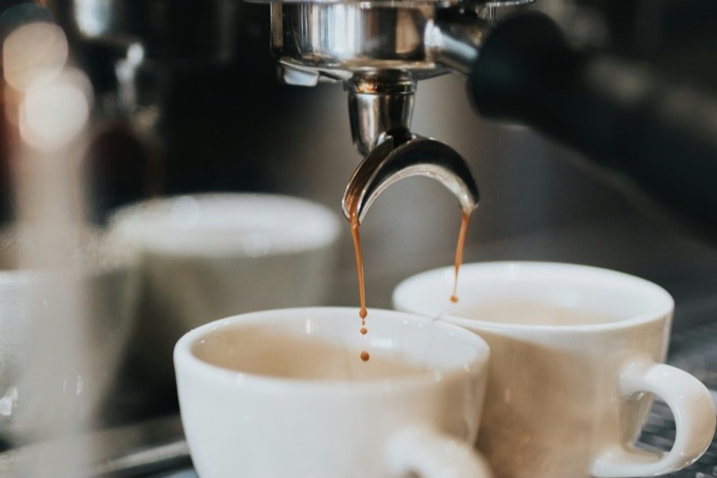 Double espresso shot being pulled from a spouted portafilter into two white demitasse cups