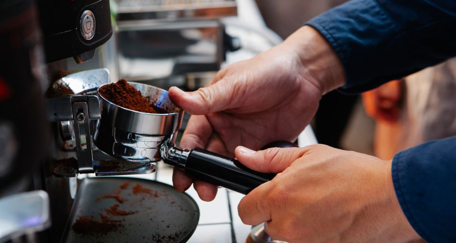 Home barista grinding coffee beans with entry-level espresso grinder on counter