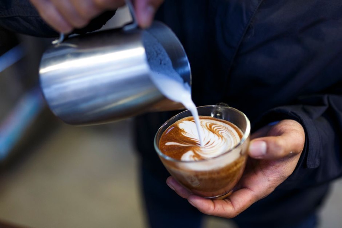 Barista holding 12oz stainless steel milk pitcher during espresso pour, showing grip position