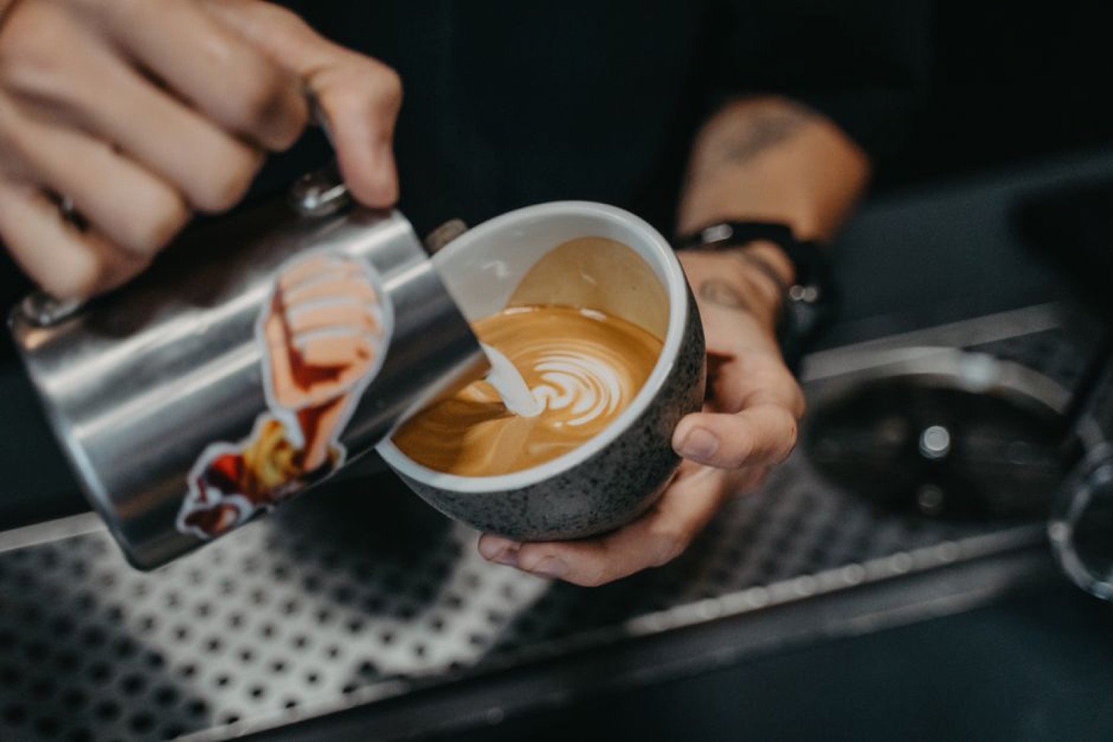 Barista pouring steamed milk into espresso cup to create latte art pattern