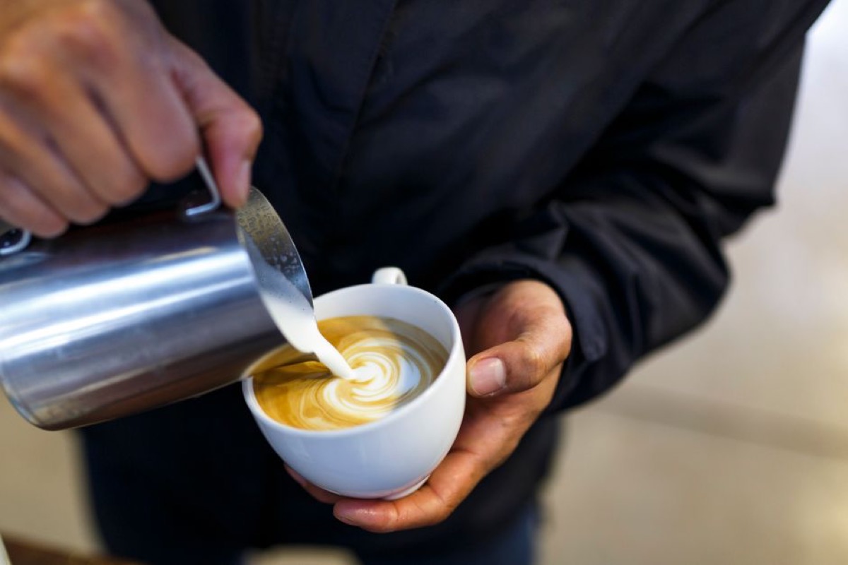 Barista completing pour of detailed rosetta pattern in a flat white espresso drink