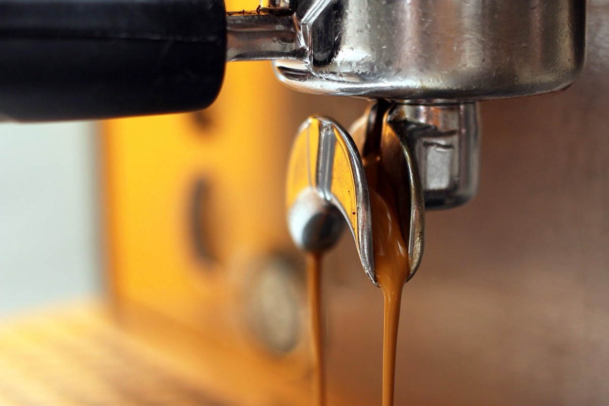 Close-up espresso extraction showing caramel-colored flow from portafilter into glass
