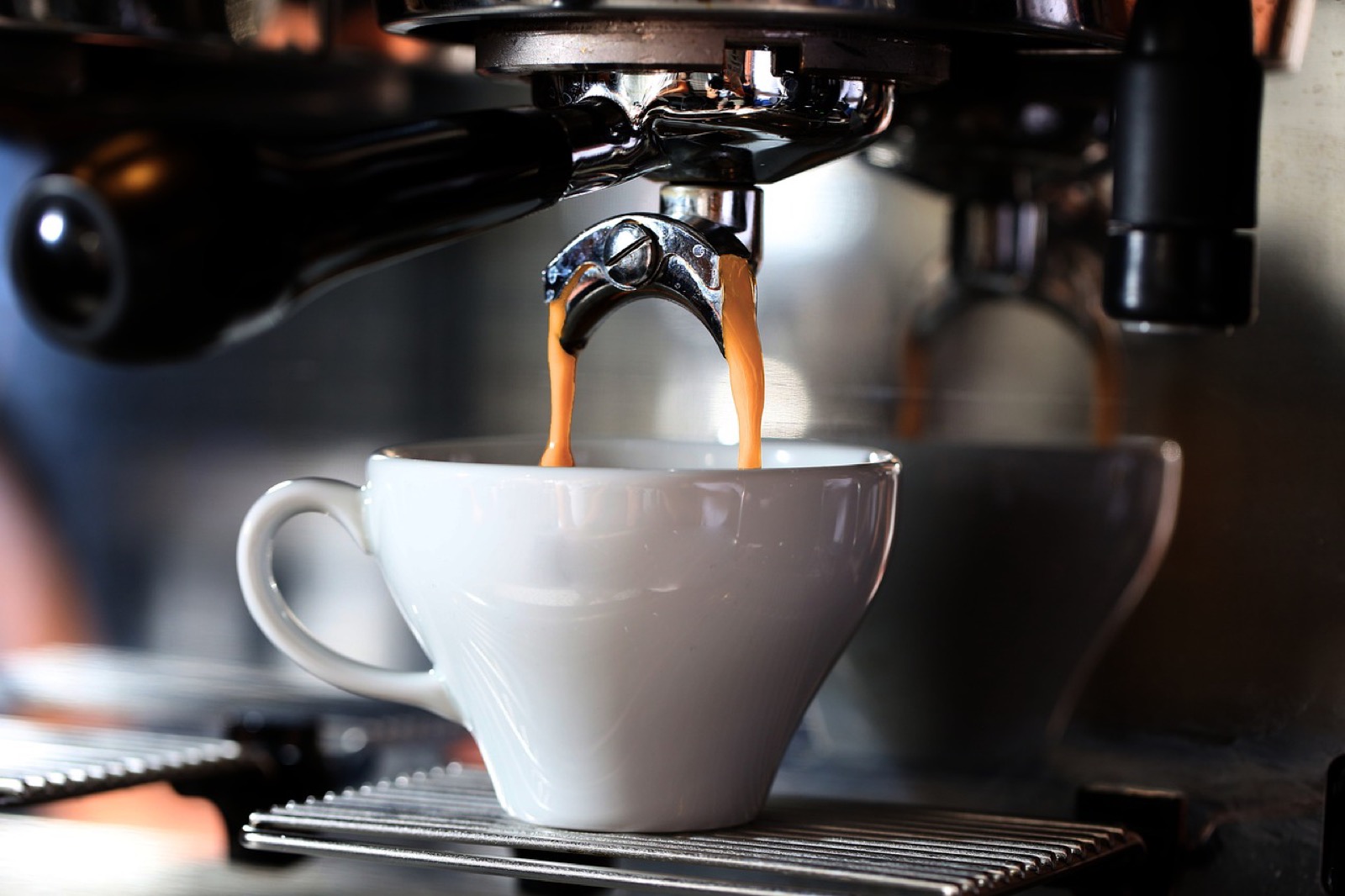 Espresso extraction showing twin streams and crema formation from group head into white cup